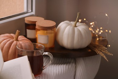 Photo of Beautiful pumpkins, tea and candles on window sill indoors