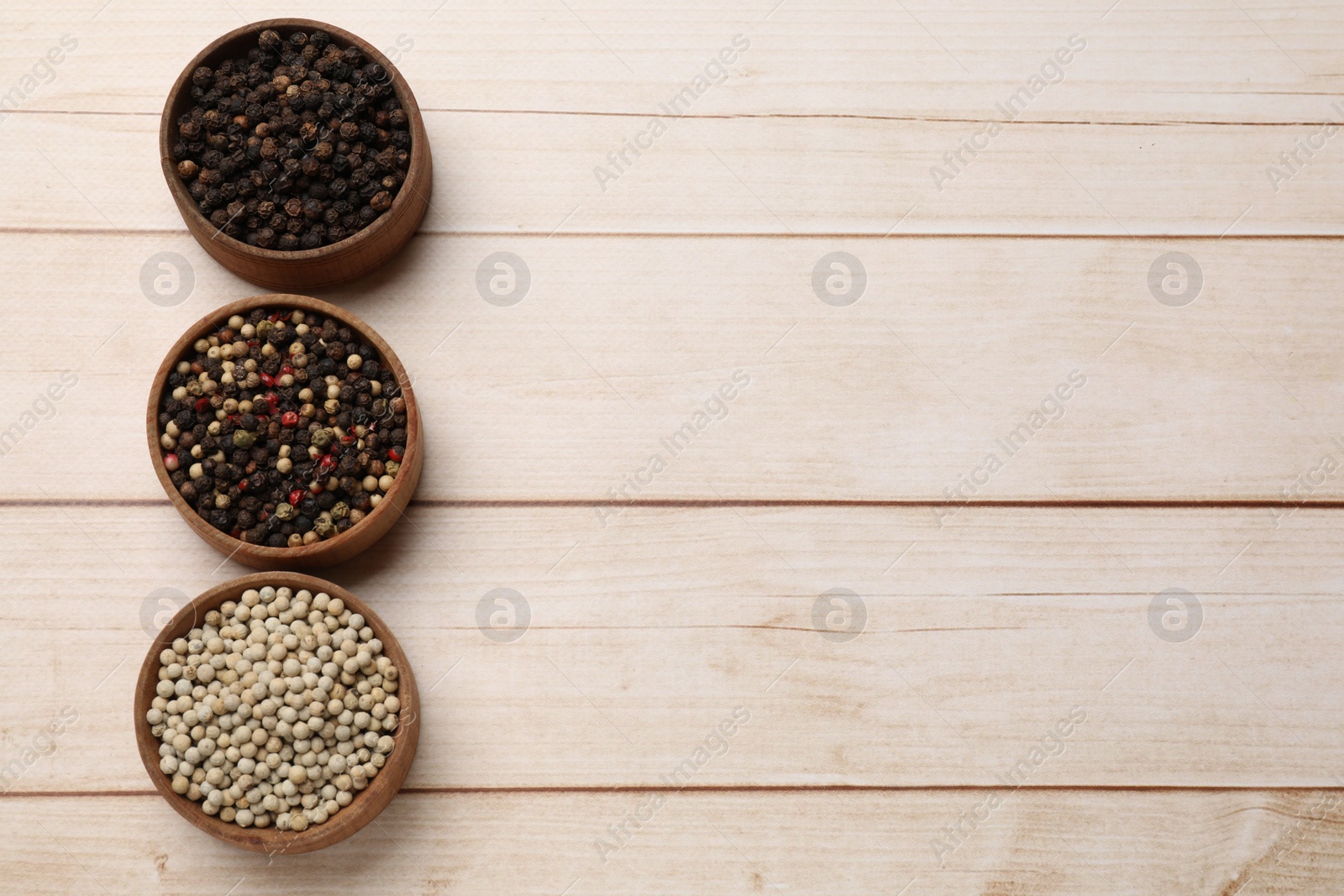 Photo of Aromatic spices. Different peppers in bowls on wooden table, flat lay. Space for text