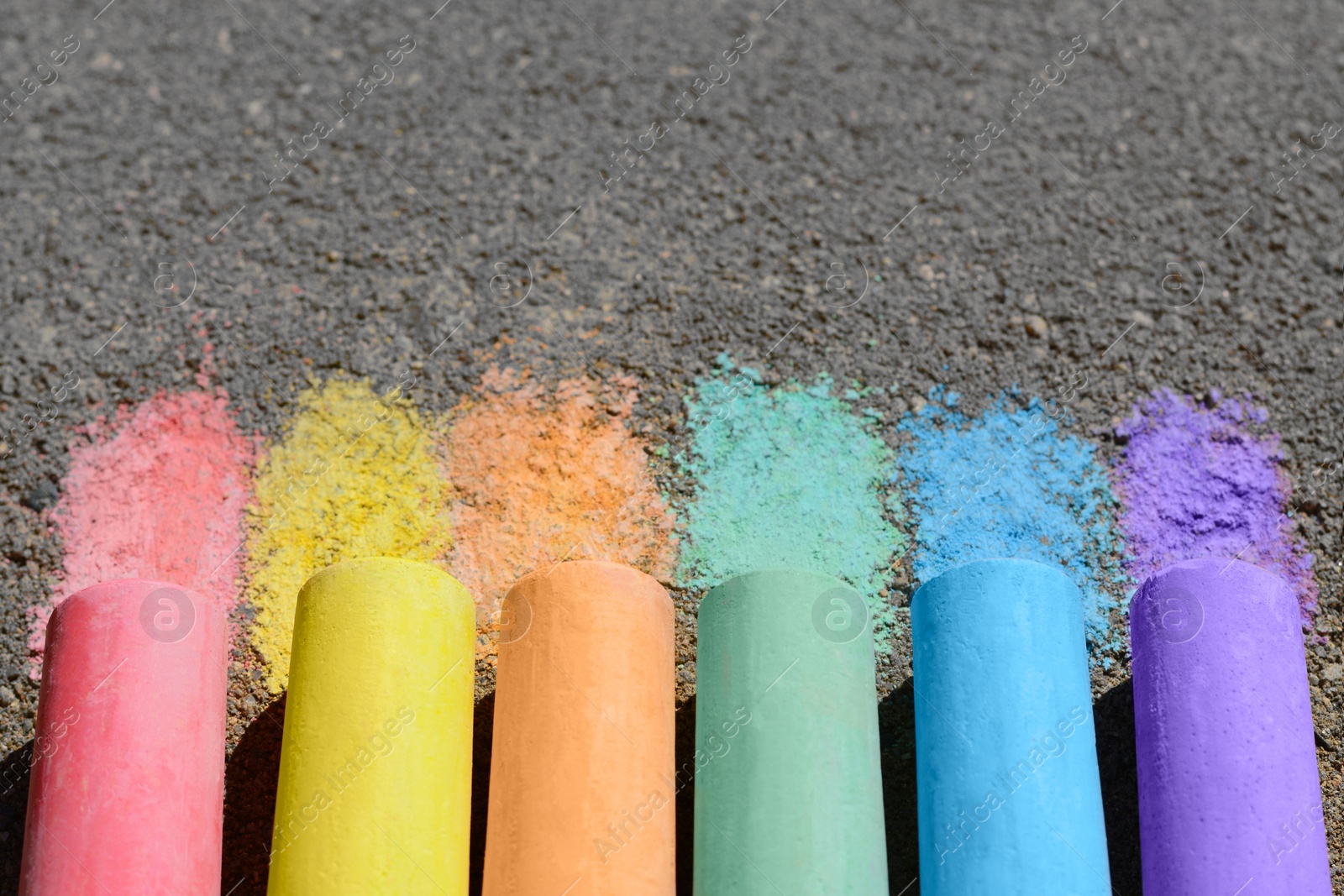 Photo of Colorful chalk sticks on asphalt outdoors, closeup. Space for text