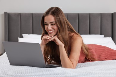 Happy woman with laptop on bed in bedroom