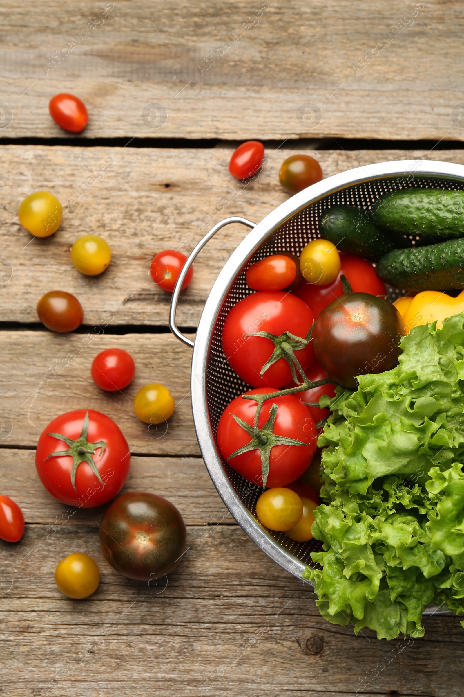 Photo of Fresh vegetables in colander on wooden table, flat lay