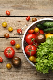 Fresh vegetables in colander on wooden table, flat lay