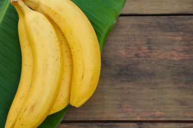 Photo of Delicious bananas and green leaf on wooden table, top view. Space for text