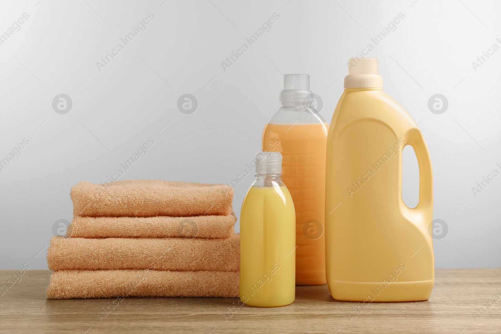 Photo of Bottles of laundry detergents and stacked fresh towels on table against white background