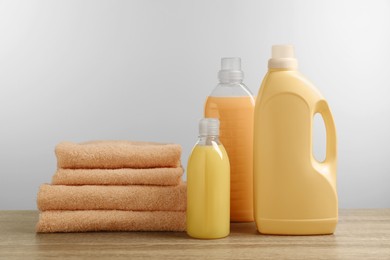 Photo of Bottles of laundry detergents and stacked fresh towels on table against white background