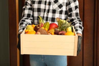 Courier holding crate with assortment of exotic fruits outdoors, closeup