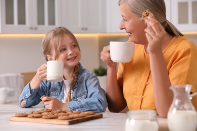 Photo of Happy grandmother with her granddaughter eating cookies in kitchen