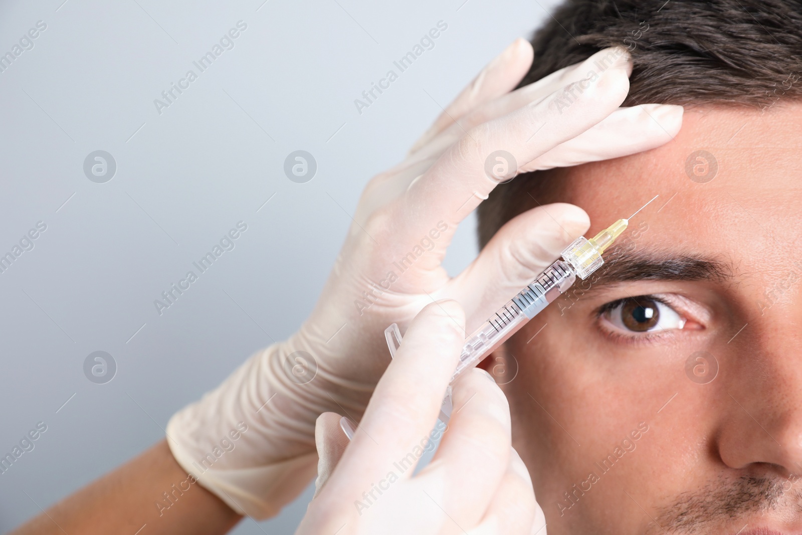 Photo of Man getting facial injection on grey background, closeup. Cosmetic surgery