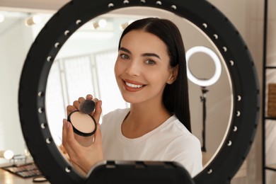 Beautiful young woman with face powder and brush indoors, view through ring lamp
