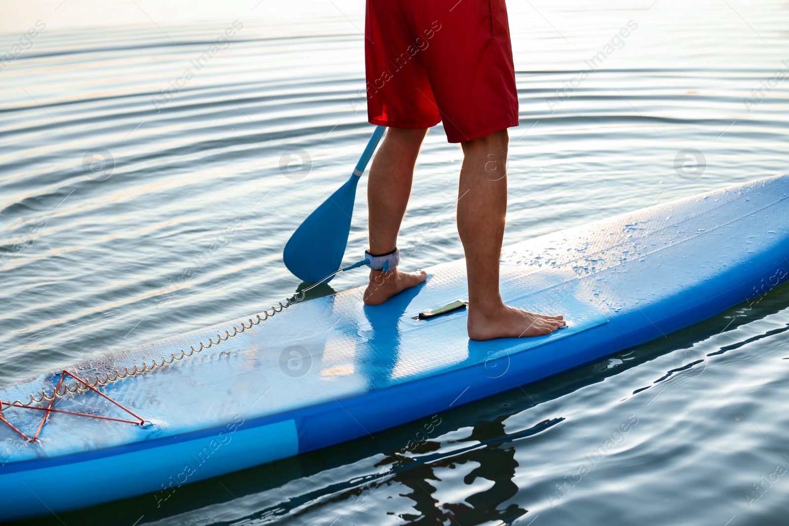 Photo of Man paddle boarding on SUP board in river at sunset, closeup