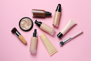 Photo of Liquid foundations and beauty accessories on pink background, flat lay