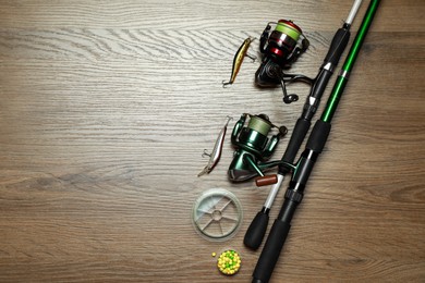 Fishing rods with spinning reels and baits on wooden background, flat lay. Space for text