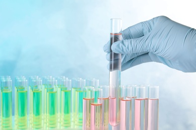 Photo of Scientist taking test tube with liquid sample on color background, closeup