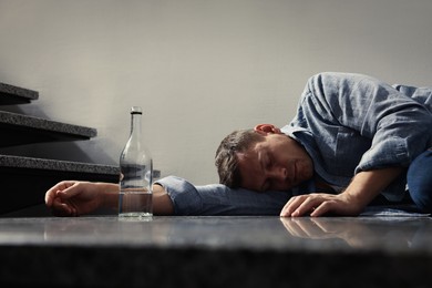 Addicted man with alcoholic drink sleeping on floor indoors