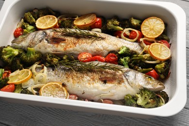 Photo of Delicious fish with vegetables and lemon in baking dish on table