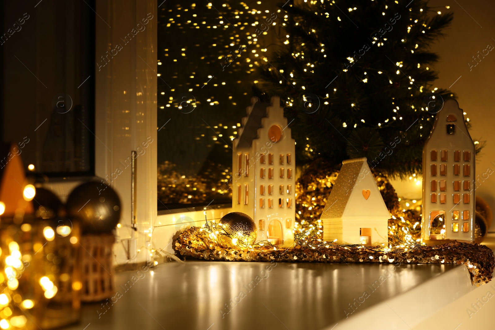 Photo of Beautiful decorative houses, baubles and small Christmas tree on window sill indoors