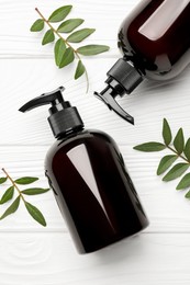 Photo of Shampoo bottles and green leaves on white wooden table, flat lay