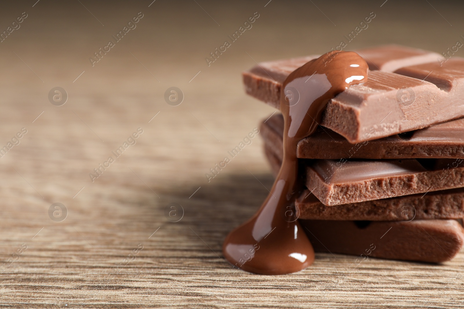 Photo of Pieces of milk chocolate with tasty paste on wooden table, closeup. Space for text