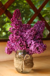 Beautiful lilac flowers in glass jar on wooden table indoors