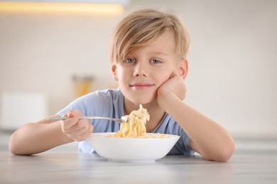 Photo of Happy boy eating tasty pasta at table in kitchen