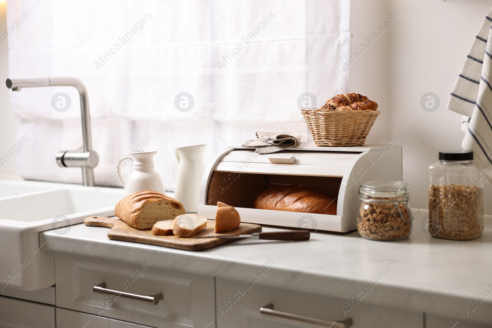 Photo of Wooden bread basket with freshly baked loaves on white marble table in kitchen