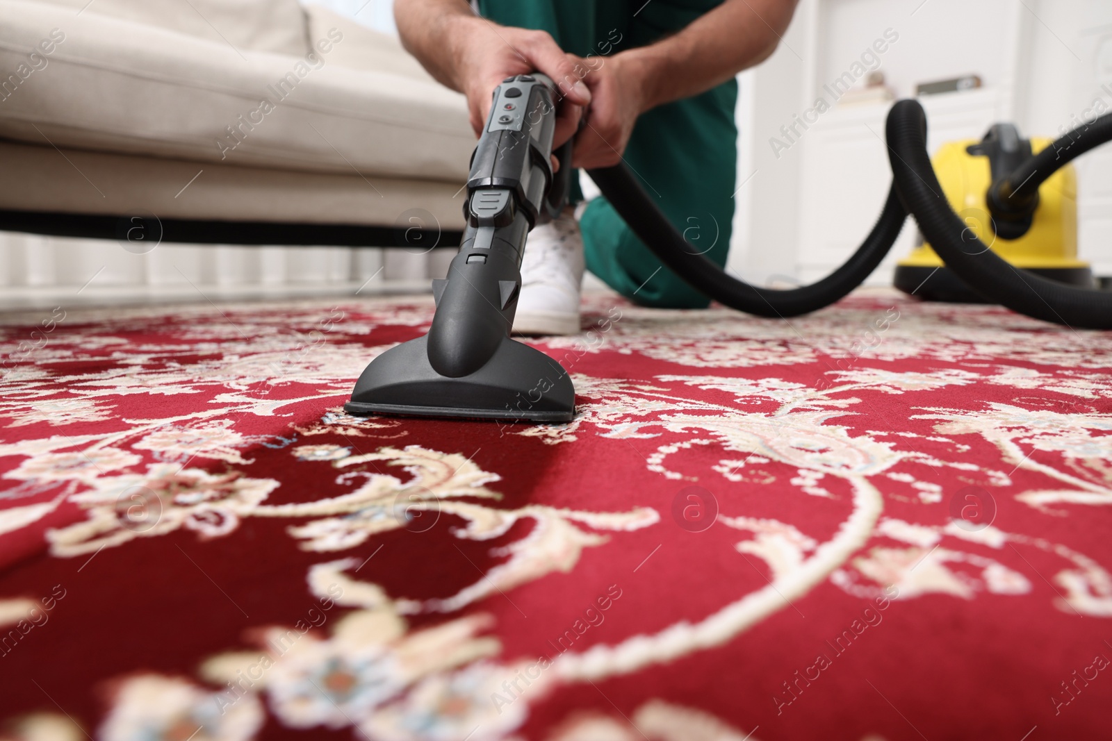 Photo of Dry cleaner's employee hoovering carpet with vacuum cleaner indoors, selective focus