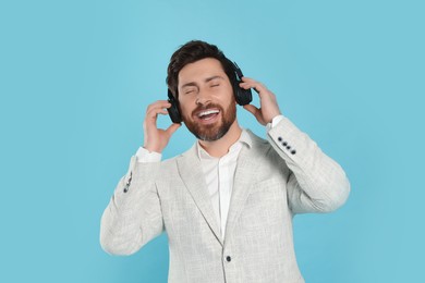 Photo of Happy man listening music with headphones on light blue background