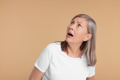 Portrait of surprised senior woman on beige background, space for text