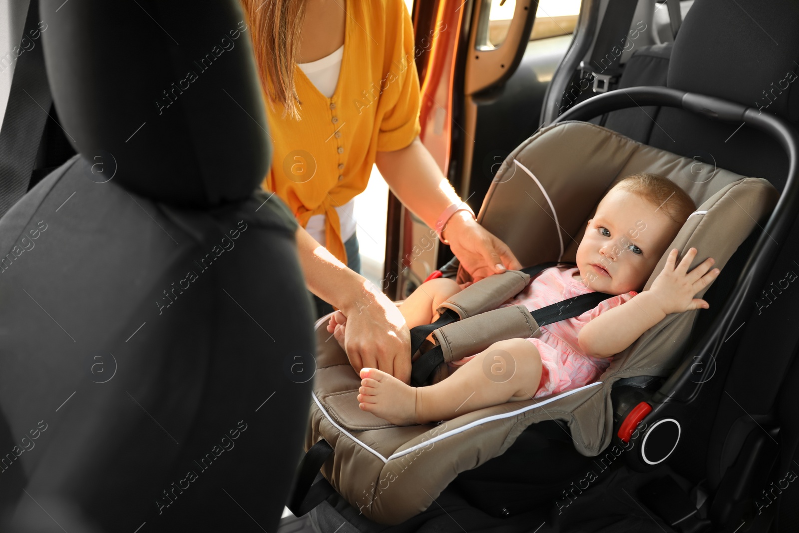 Photo of Mother fastening baby to child safety seat inside of car