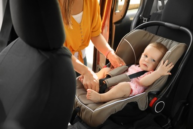 Mother fastening baby to child safety seat inside of car