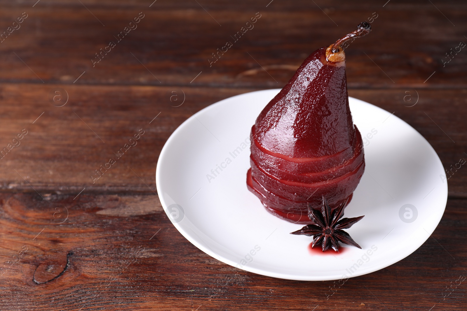 Photo of Tasty red wine poached pear and anise on wooden table, closeup. Space for text