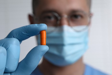 Doctor holding pill on light background, selective focus. Space for text