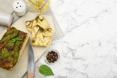 Photo of Freshly baked pesto bread with basil served on white marble table, flat lay. Space for text