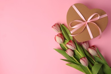 Heart shaped gift box with bow and beautiful tulips on pale pink background, flat lay. Space for text