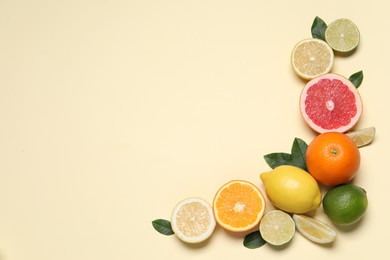 Different cut citrus fruits and leaves on beige table, flat lay. Space for text