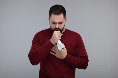 Photo of Sick man with tissue coughing on gray background