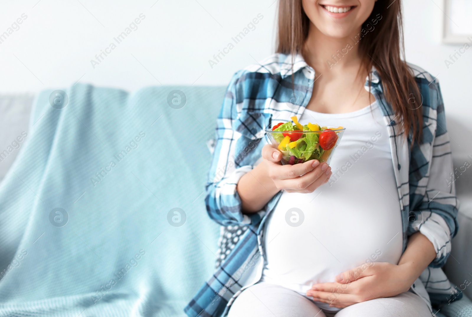 Photo of Young pregnant woman with vegetable salad on sofa at home