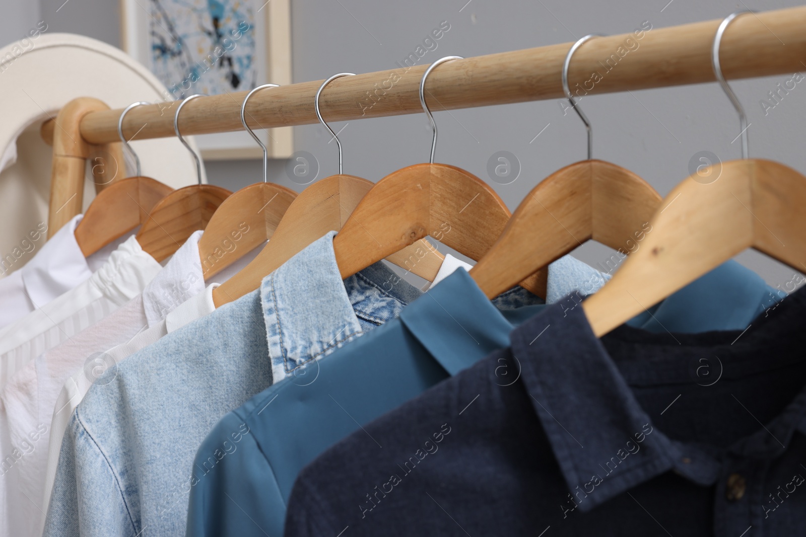 Photo of Rack with different stylish shirts on wooden hangers against grey background, closeup. Organizing clothes