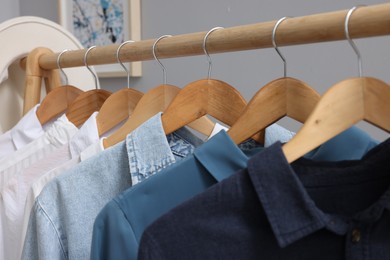 Rack with different stylish shirts on wooden hangers against grey background, closeup. Organizing clothes