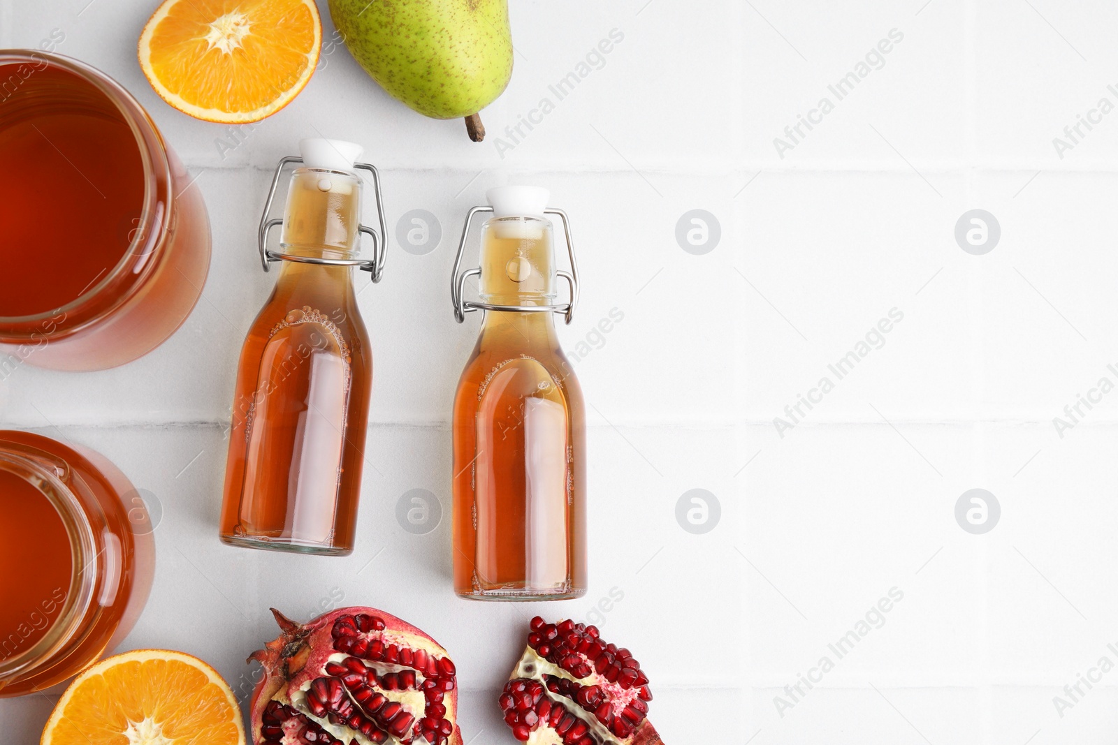 Photo of Tasty kombucha and fresh fruits on white tiled table, flat lay. Space for text