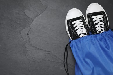 Photo of Blue drawstring bag and sneakers on grey textured background, top view. Space for text