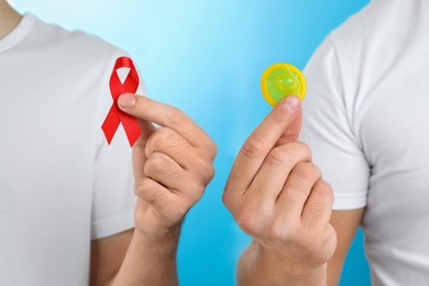 Men with condom and AIDS awareness ribbon on light blue background, closeup