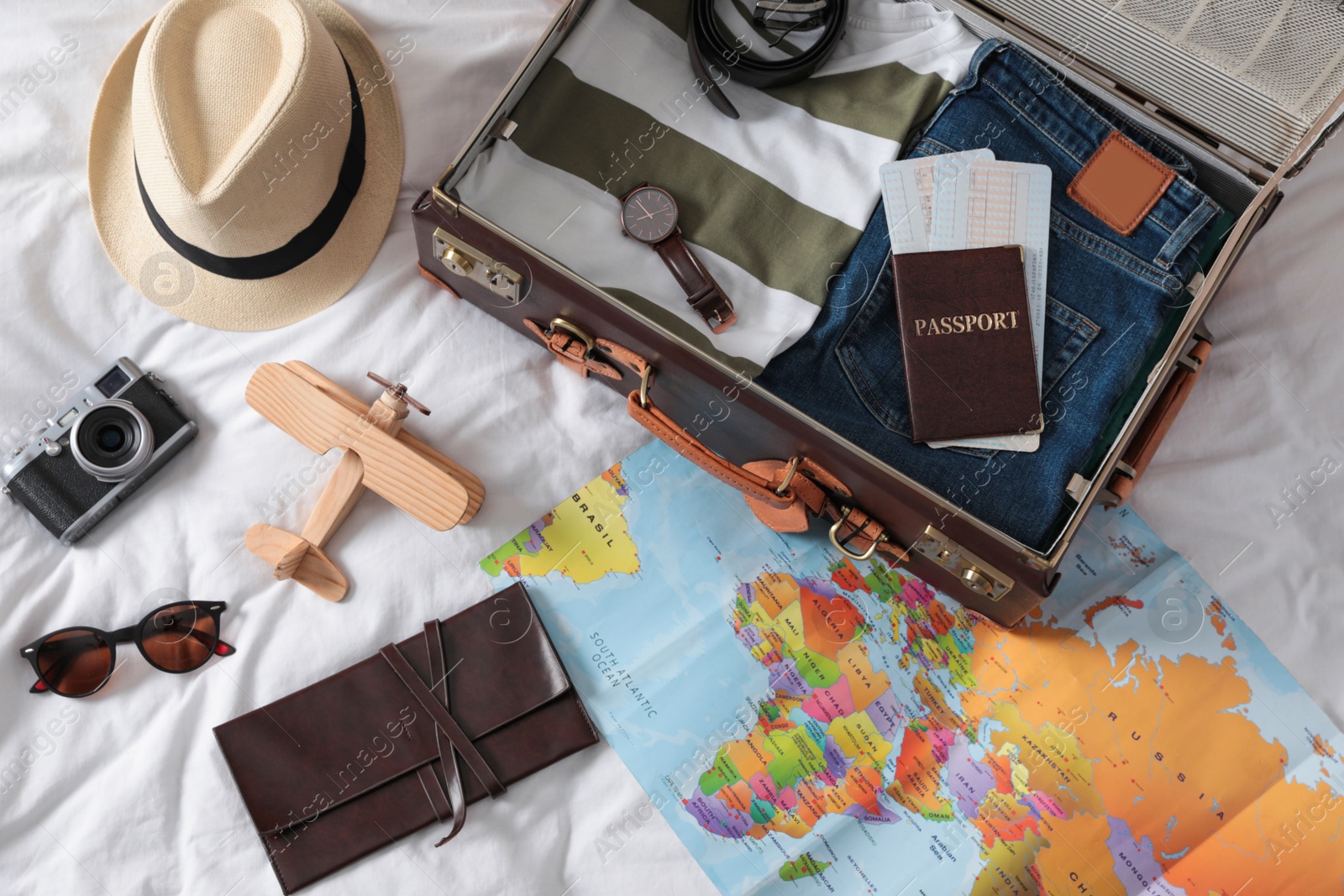 Photo of Packed suitcase and travel accessories on white fabric, above view. Summer vacation