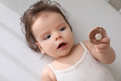 Cute little baby with pacifier in comfortable crib, top view