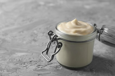 Photo of Tasty mayonnaise in jar on gray textured table, closeup. Space for text