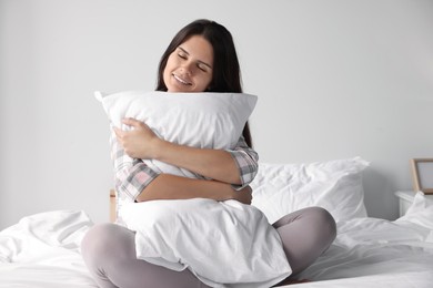 Beautiful young woman hugging pillow on bed at home