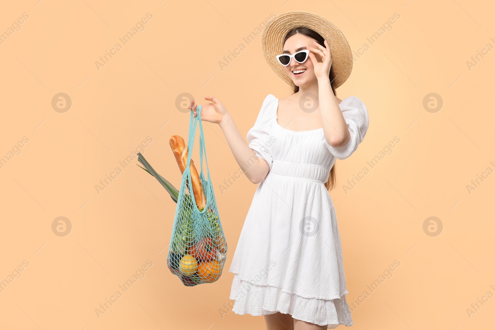 Photo of Woman with string bag of fresh vegetables and baguette on beige background, space for text