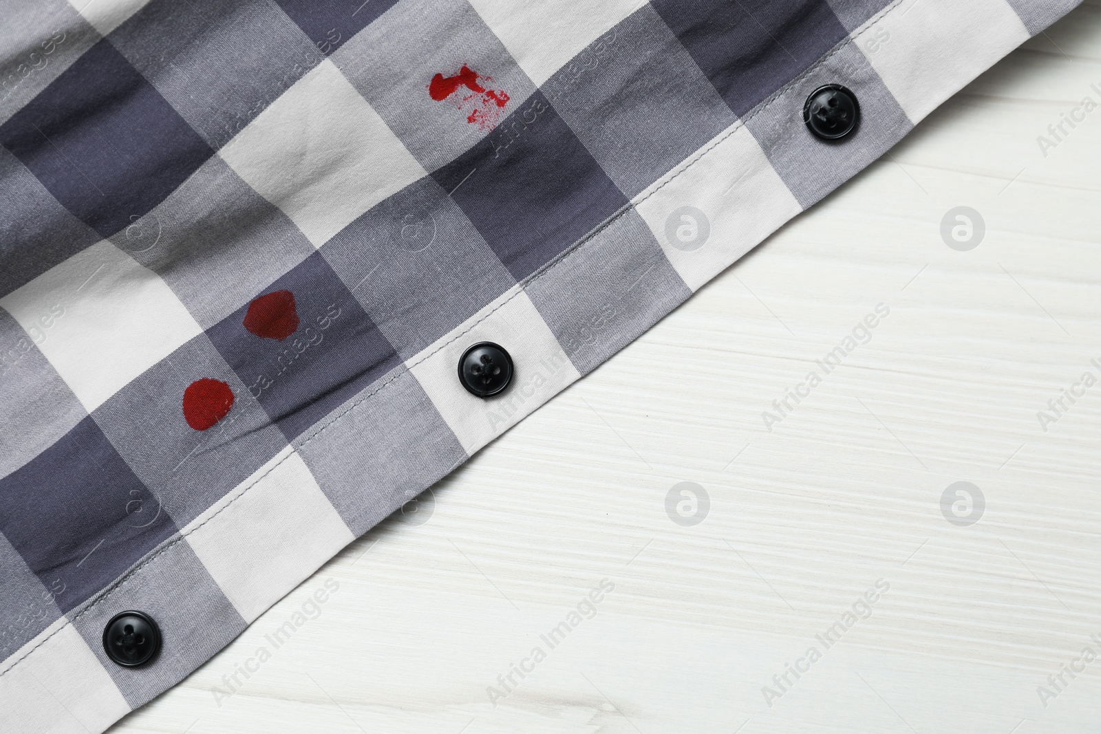 Photo of Shirt with stain of red ink on wooden table, top view. Space for text