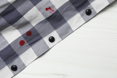 Shirt with stain of red ink on wooden table, top view. Space for text