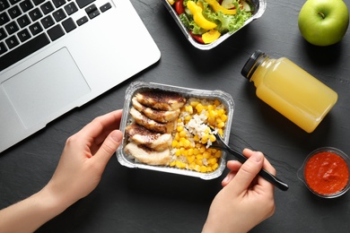 Photo of Woman eating from lunchbox at grey table, closeup. Healthy food delivery